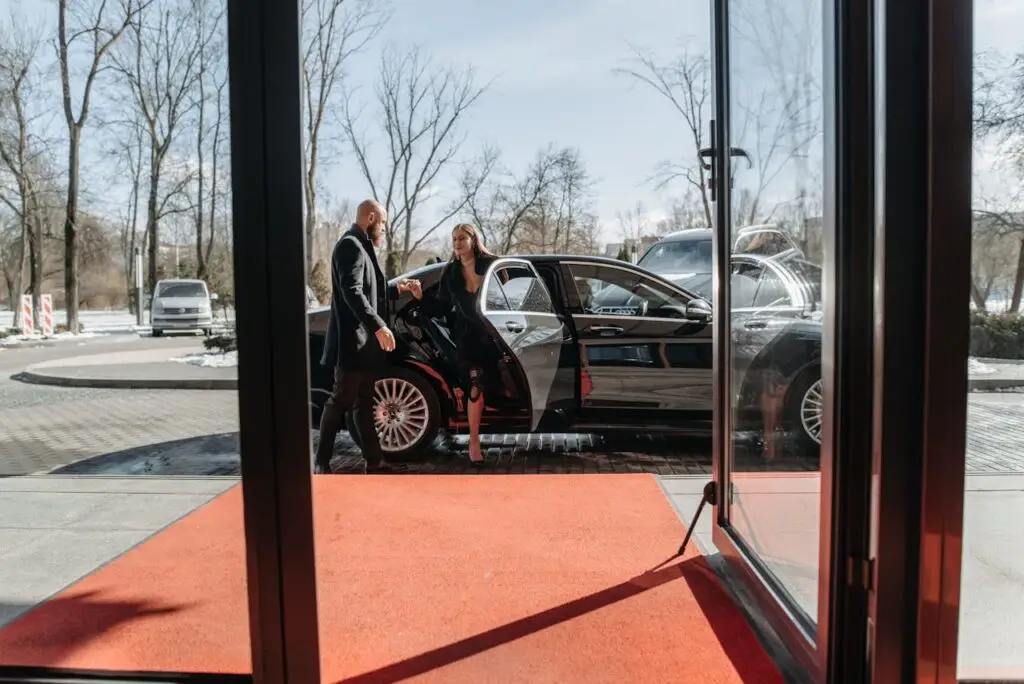 A couple stepping out of a luxury car onto a red carpet in an upscale outdoor setting.