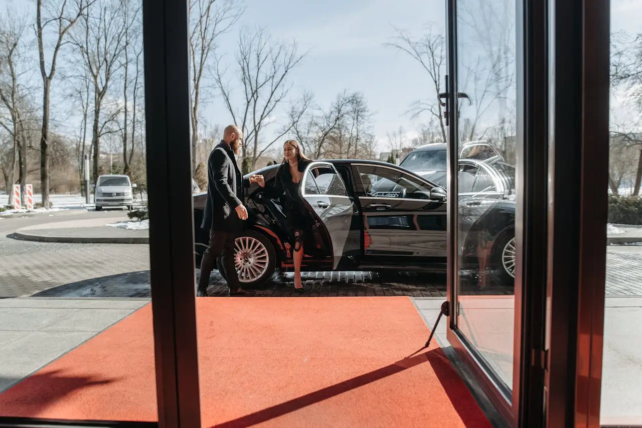 A couple stepping out of a luxury car onto a red carpet in an upscale outdoor setting.